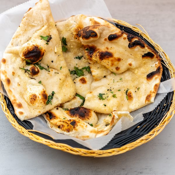 Golden-brown Indian naan bread, garnished with fresh herbs, served in a black and gold woven basket.