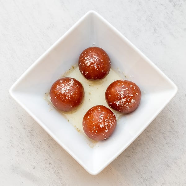 Four gulab jamun, Indian fried dough balls in syrup, garnished with coconut flakes in a white bowl.