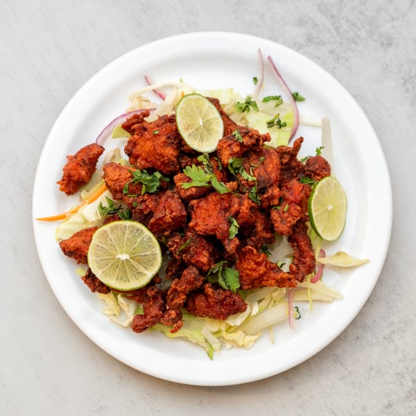 Indian Spice's Chicken 65, a vibrant red fried chicken dish with lime wedges and cilantro.